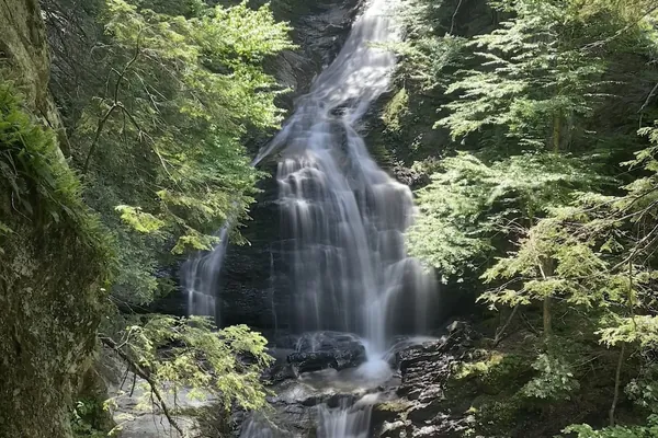 Moss Glen Falls in Stowe, Vermont, cascading over dark rock ledges in a wooded gorge in summer.