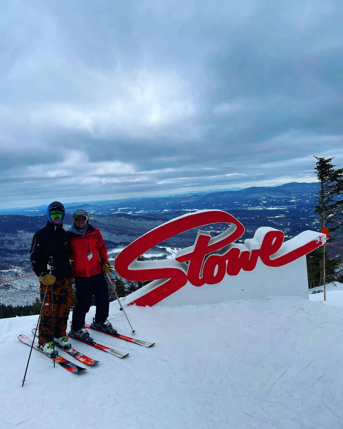 Two skiers beside the Stowe sign at the top of the mountain